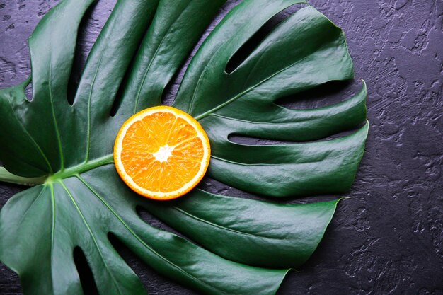 Une orange sur une feuille tropicale verte Plante d'intérieur Monstera sur fond noir Photo écologique