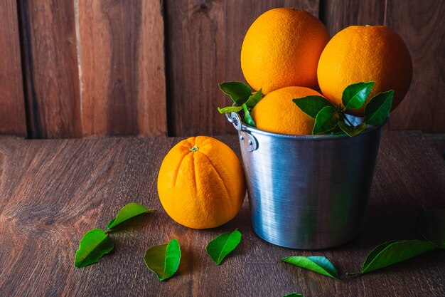 Orange fraîche dans un panier en aluminium sur fond en bois.