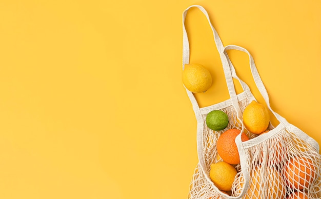 Oranges, citrons, citrons verts et pamplemousses frais dans un sac en filet sur fond jaune