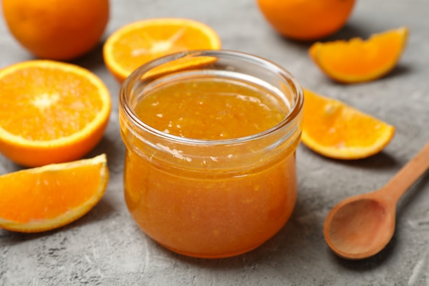 Oranges, cuillère et pot en verre avec de la confiture sur fond gris, Close up