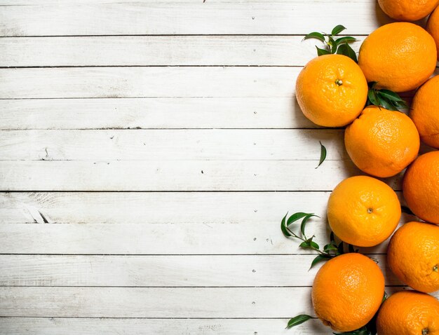 Oranges fraîches avec des feuilles sur une table en bois blanc