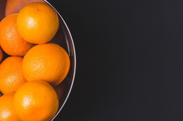 Oranges fraîches juteuses dans un bol en acier sur fond noir. Agrumes. Fruits à la vitamine C