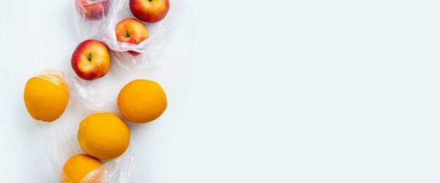 Des oranges fraîches mûres, des pommes dans des sacs transparents sur un fond blanc.