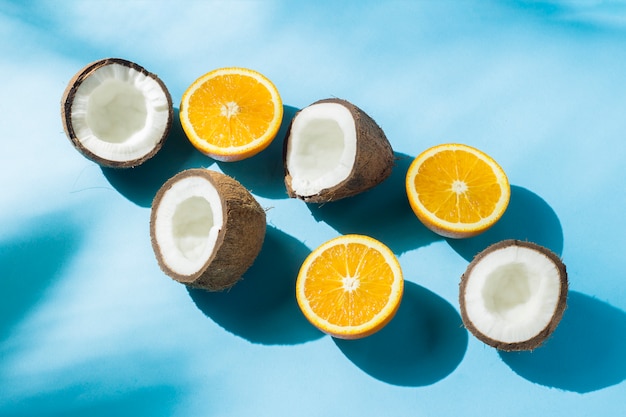 Oranges et noix de coco sur une surface bleue sous lumière naturelle avec des ombres. Lumière forte. Concept de régime alimentaire, alimentation saine, vacances sous les tropiques, vacances et voyages.