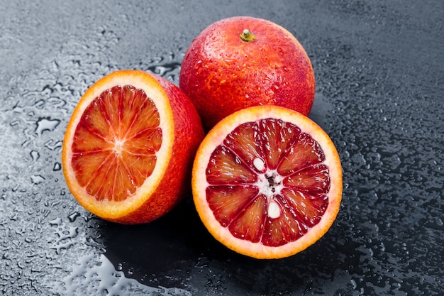 Oranges sanglantes entières et coupées en deux sur une ardoise noire avec des gouttes d'eau, des fruits rouges orange sicilienne.