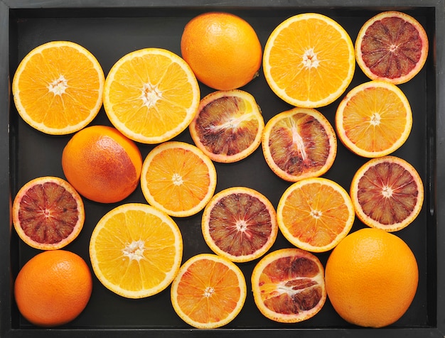 Oranges sanguines entières et coupées en deux sur un plateau noir