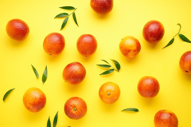 Oranges sanguines mûres avec des brins de feuilles vertes sur une vue de dessus de fond jaune