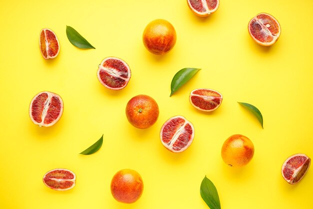 Oranges sanguines mûres tranchées et entières avec des brins de feuilles vertes sur une vue de dessus de fond jaune