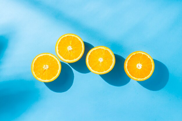 Oranges sur une surface bleue sous lumière naturelle avec des ombres. Lumière forte. Concept de régime alimentaire, alimentation saine, repos sous les tropiques, vacances et voyages, vitamines. Mise à plat, vue de dessus.