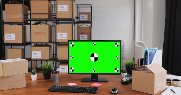 Ordinateur de bureau avec maquette d'affichage chromakey à écran vert se dresse sur le bureau dans l'entrepôt Boîtes en carton en arrière-plan