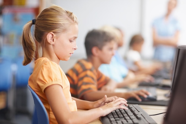 L'ordinateur et la fille en classe, la frappe et Internet avec évaluation en ligne, l'enfance en groupe et les enfants en classe, l'ordinateur ou la recherche pour une tâche de projet ou des connaissances avec un test ou un apprentissage.