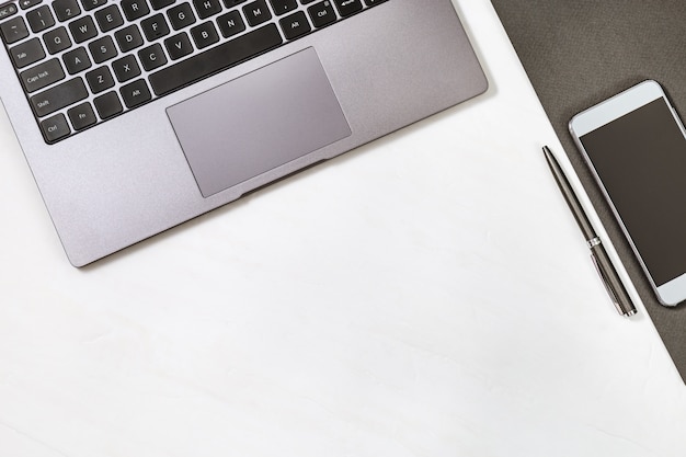 Ordinateur gris, stylo et smartphone sur table.