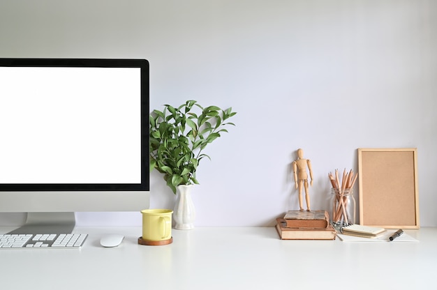 Ordinateur PC sur l’espace de travail avec une tasse de café, un crayon, des livres et une plante sur le bureau.