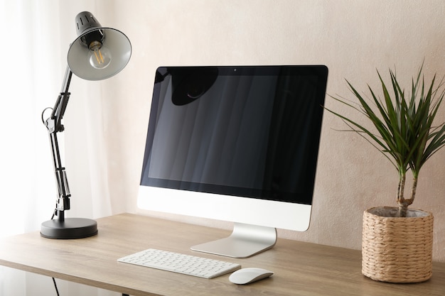 Ordinateur, plante et lampe sur table en bois. Salle de travail