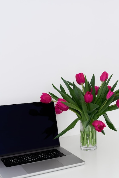 Ordinateur portable et bouquet de fleurs de tulipes fraîches dans un vase sur un tableau blanc