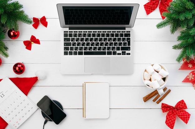 Photo ordinateur portable sur un bureau en bois blanc entouré de décorations de noël rouges, vue de dessus