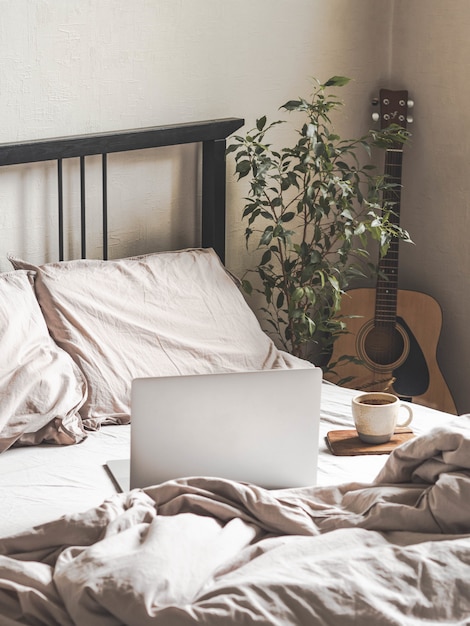 Ordinateur portable et café sur le lit et une guitare à côté du lit dans la chambre