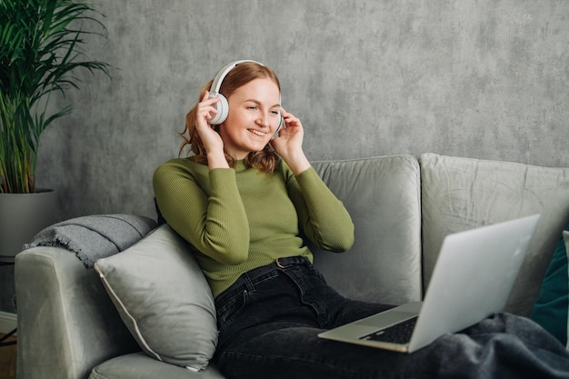 Ordinateur portable casque et femme sur un canapé à la maison écoutant de la musique ou de l'audio tout en diffusant en ligne calme f