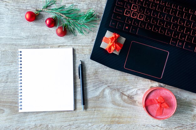 Ordinateur portable, coffrets cadeaux, cahier et décorations de Noël sur table en bois. Mise à plat