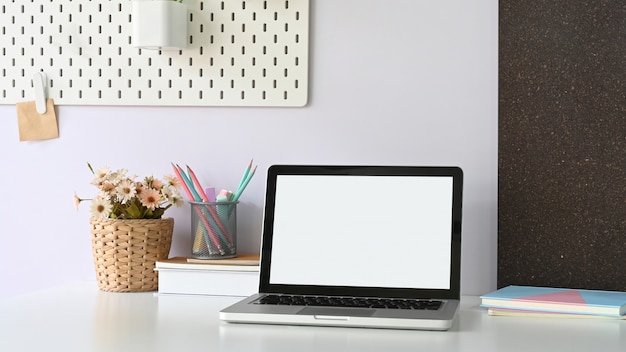 Un ordinateur portable à écran blanc blanc met sur un bureau de travail blanc entouré de matériel de bureau.