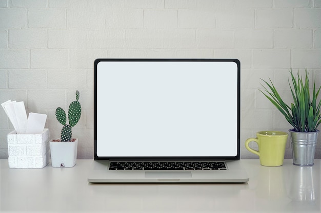 Ordinateur portable à écran blanc avec cactus vert, tasse et boîte de carte blanche sur la table supérieure blanche.