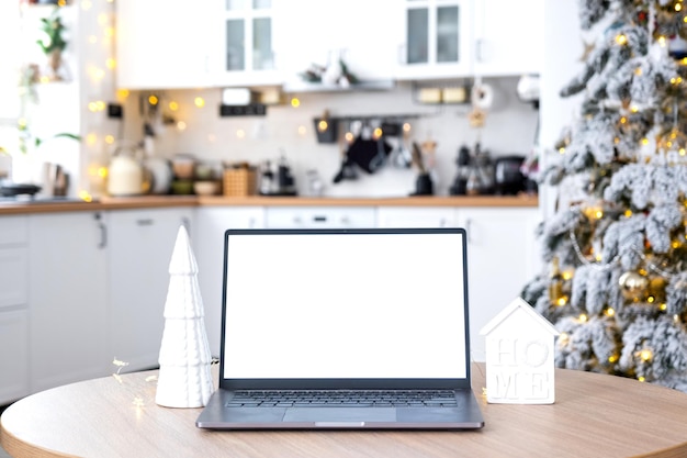 Un ordinateur portable avec un écran blanc dans la cuisine de Noël décorée en blanc confortable