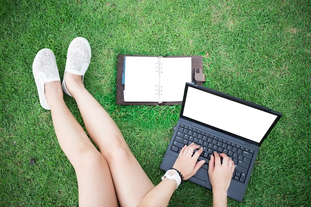 Ordinateur portable avec écran blanc de mode de vie de femme assis au parc