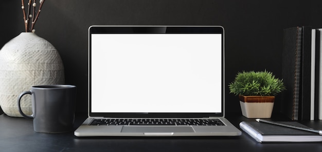 Ordinateur portable à écran blanc ouvert dans une salle de bureau moderne sombre avec des fournitures de bureau