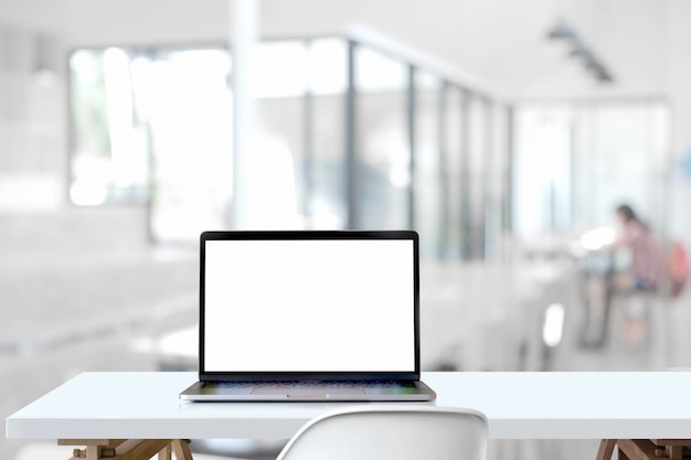 ordinateur portable à écran blanc sur une table en bois dans un espace de travail partagé.