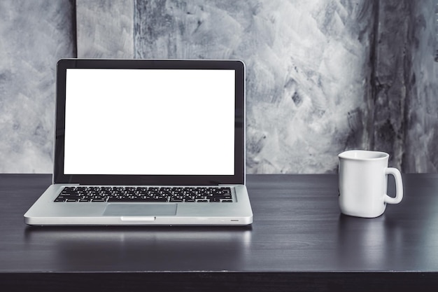 Un ordinateur portable avec un écran blanc et une tasse de café blanche sur le bureau