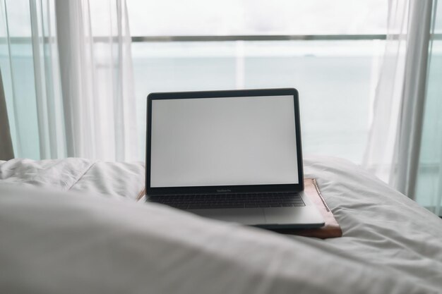 Ordinateur portable à écran vide de concept de travail sur le lit et le balcon avec vue sur l'océan