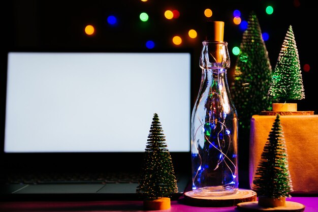 Ordinateur portable avec écran vide sur table en bois, arbre de Noël flou et cadeaux sur fond. Carte de Noël et bonne année, bokeh, étincelles. Mise à plat, vue de dessus