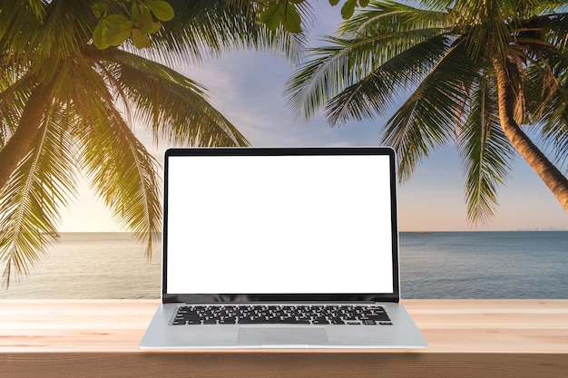 Ordinateur portable à écran vide sur une table en bois avec cocotier et coucher de soleil sur la plage tropicale Concept de vacances d'été
