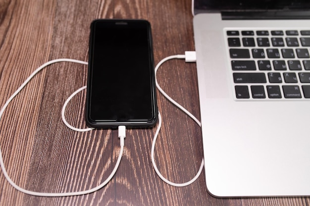 Un ordinateur portable est branché sur un chargeur avec un téléphone branché dessus.