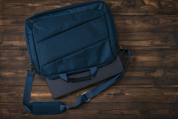 Un ordinateur portable fermé dépasse d'un sac bleu sur une table en bois Accessoires pour étudier et travailler