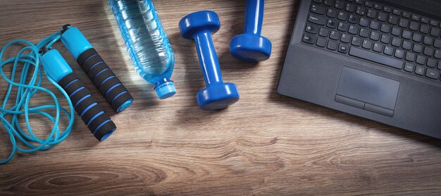 Ordinateur portable haltères corde à sauter bouteille d'eau sur le fond en bois Entraînement de fitness en ligne