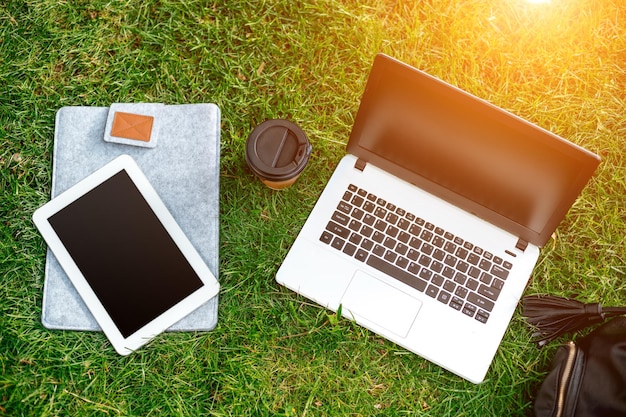 Ordinateur portable sur l'herbe verte avec sac de tasse de café et tablette dans un parc extérieur