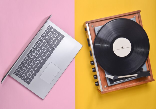 Ordinateur portable, lecteur de vinyle sur fond pastel coloré. Technologie moderne et obsolète, vue de dessus