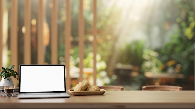 Un ordinateur portable avec une maquette d'écran blanc sur une table en bois rustique dans un beau jardin de café