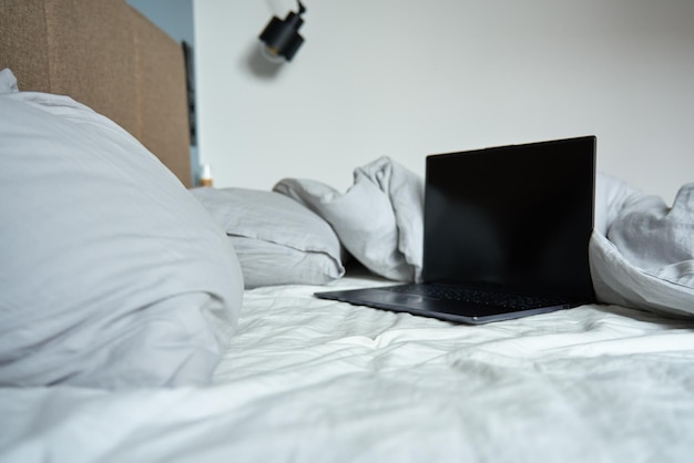 Ordinateur portable ouvert dans un lit défait avec des oreillers et des draps froissés le matin