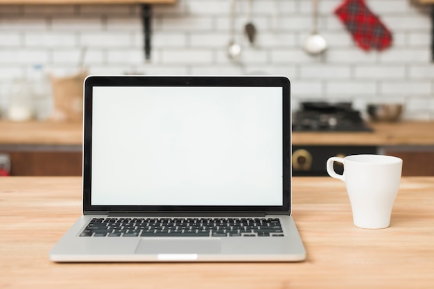 Photo un ordinateur portable ouvert avec un écran blanc et une tasse de café sur la table en bois dans la cuisine