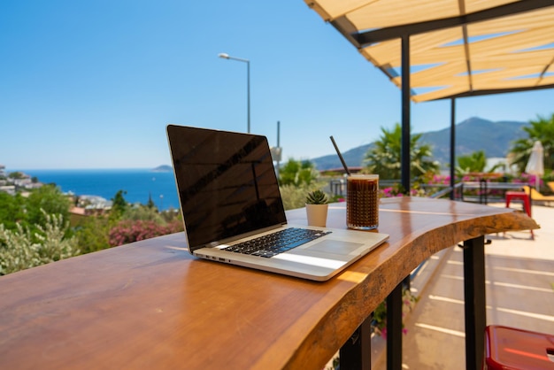 Ordinateur portable ouvert avec écran noir sur table en bois espace de travail à l'extérieur avec vue imprenable sur l'océan. La