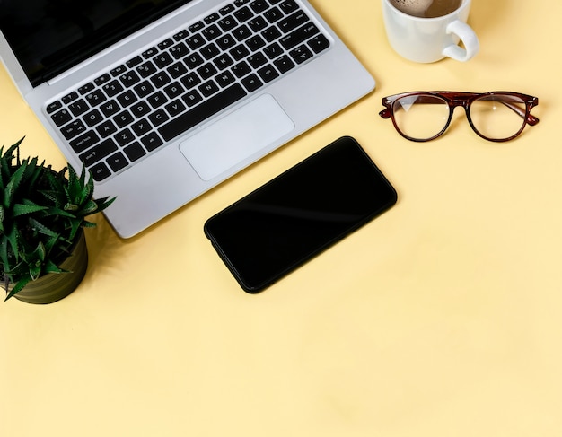 Ordinateur portable placé sur une table jaune du lieu de travail avec une tasse de café, espace de travail vide