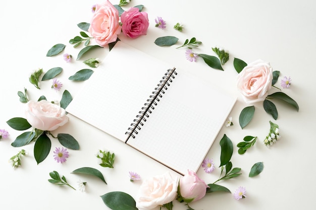 Ordinateur portable à plat sur fond blanc avec des feuilles d'été, des fleurs et d'autres articles de papeterie dans un style branché