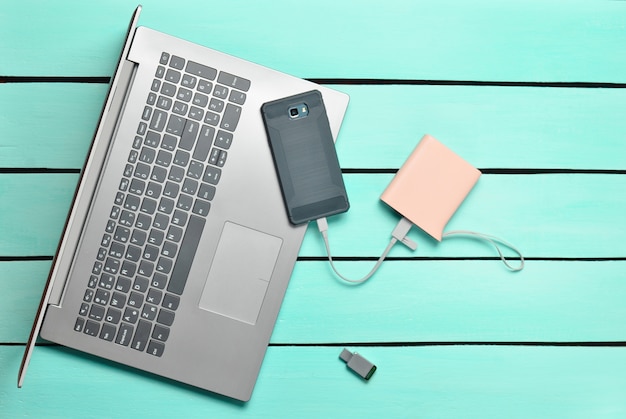 Ordinateur portable, smartphone, banque d'alimentation, clé USB sur une table en bois bleue. Appareils et gadgets numériques modernes. Vue de dessus.