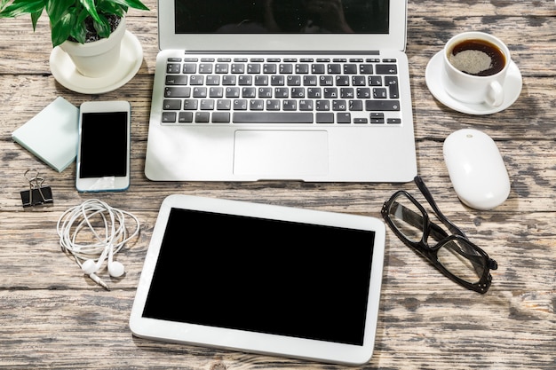 Ordinateur portable, smartphone, tablette et tasse à café avec documents financiers sur table en bois