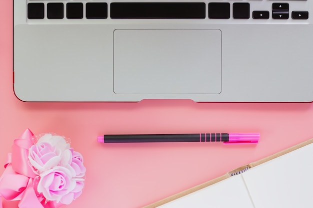 Ordinateur portable avec un stylo, un cahier ouvert et un bouquet de fleurs sur fond de couleur rose