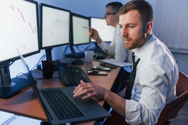 Avec un ordinateur portable sur la table Deux négociants en bourse travaillant au bureau avec la technologie d'échange