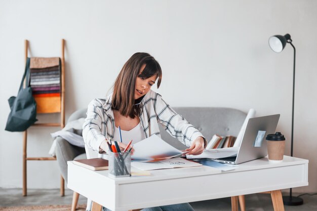 Avec un ordinateur portable sur la table La jeune travailleuse indépendante est à l'intérieur de la maison pendant la journée