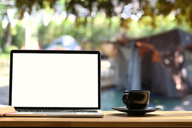 Ordinateur portable sur une table de pique-nique pliante près de la tente de camp à l'extérieur. Écran vide pour le message texte ou le contenu d'information.